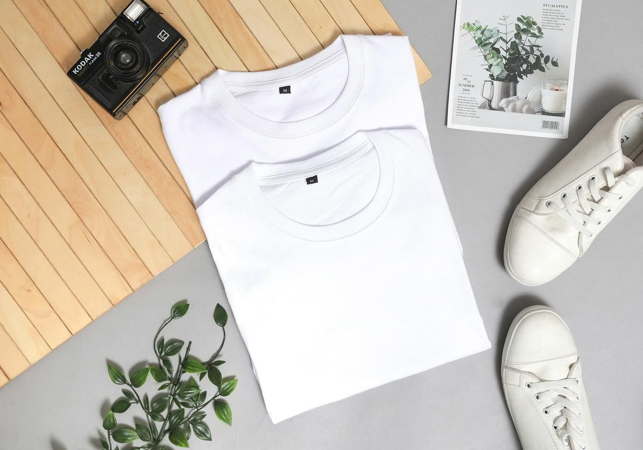 Two white t-shirts and a pair of sneakers neatly arranged on a wooden table.